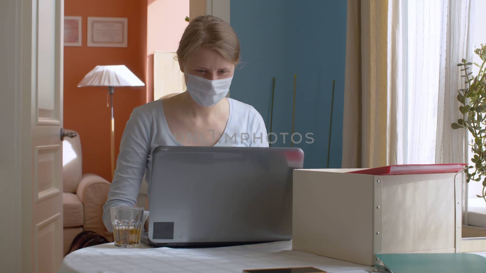 Portrait of a young attractive woman working from home. Lady in a protective mask typing on a computer. Remote work during quarantine, coronavirus epidemic. COVID-19 pandemic