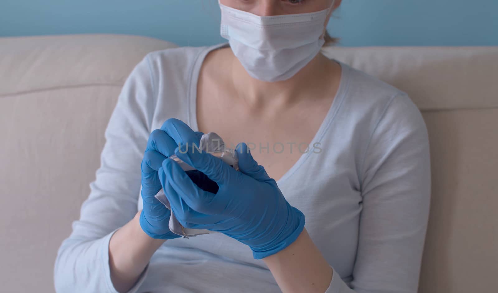 Close up woman's hands in protective gloves spraying sanitizer on the smart phone. Hygiene during epidemic. Concept of safety life. Covid-19 pandemic