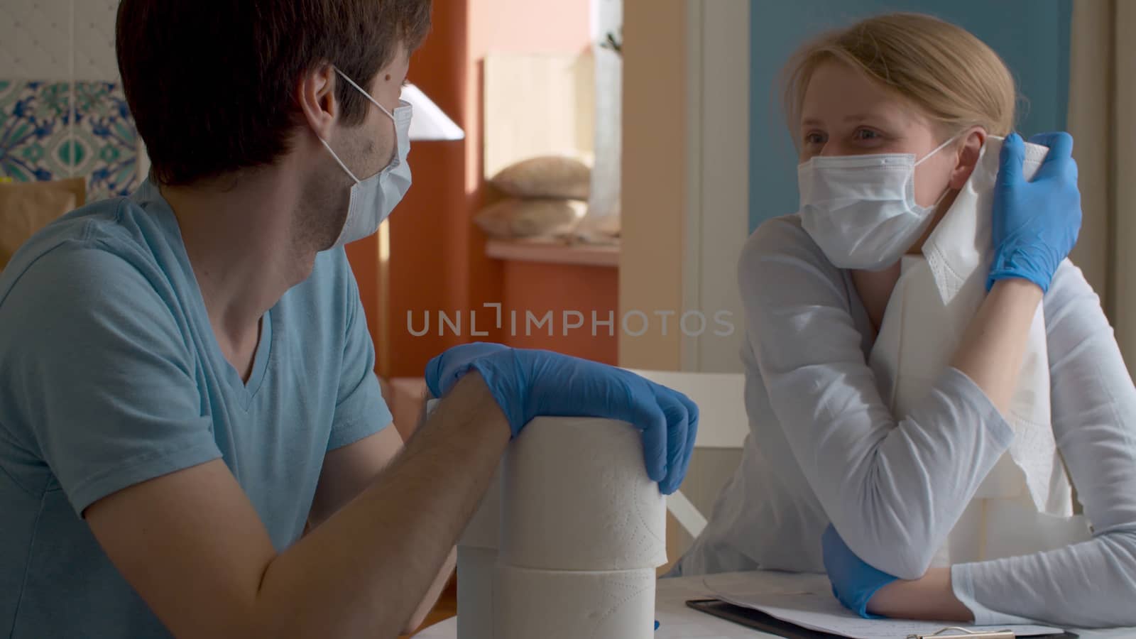 Happy family talking in bright kitchen. Wife hugging toilet paper, smiling and telling something. Husband listening to her. Coronavirus epidemic, quarantine. Covid-19 pandemic
