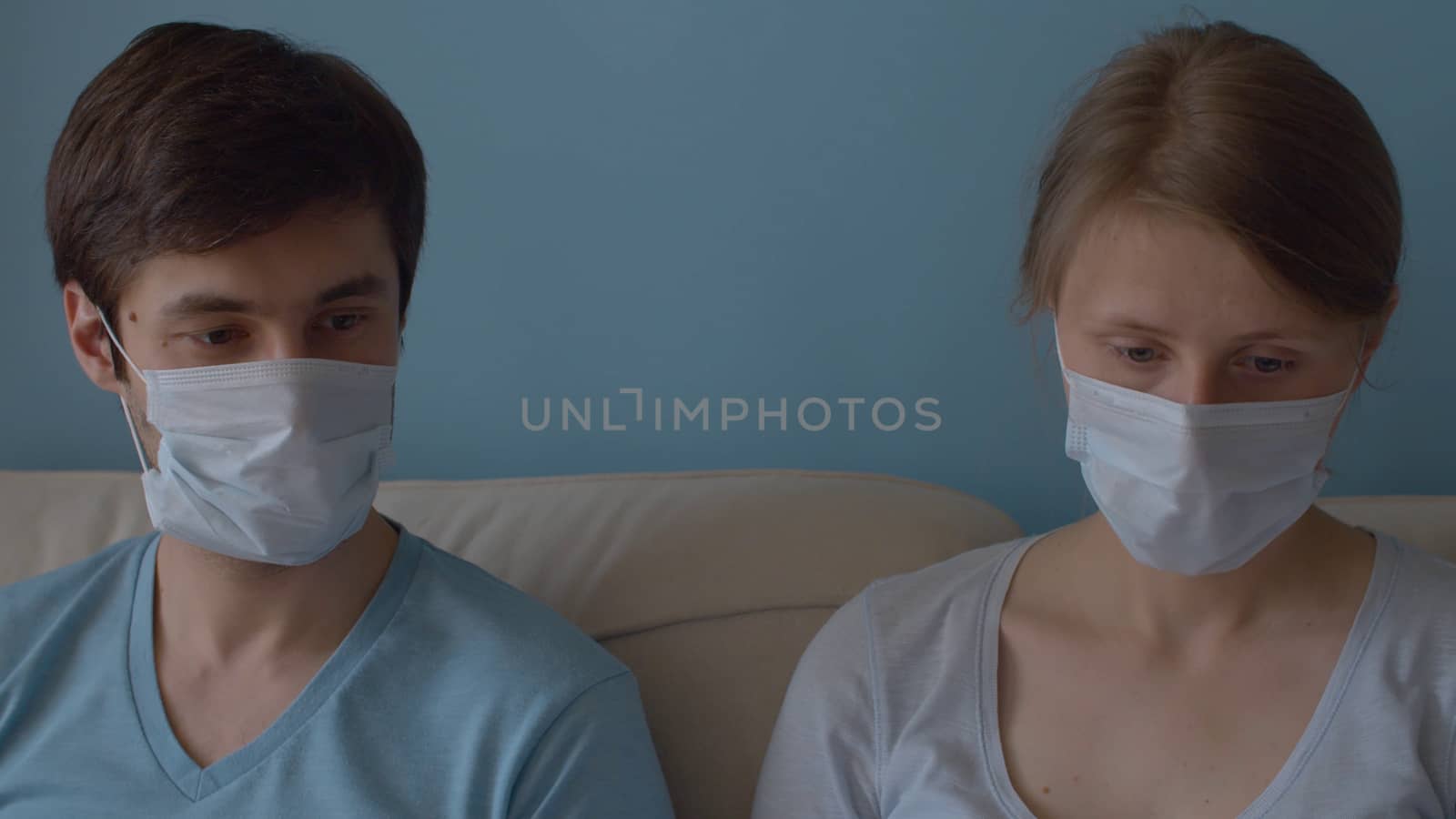 Close up portrait of couple in masks. Man and woman sitting on the sofa in bright room. Quarantine, coronavirus epidemic.