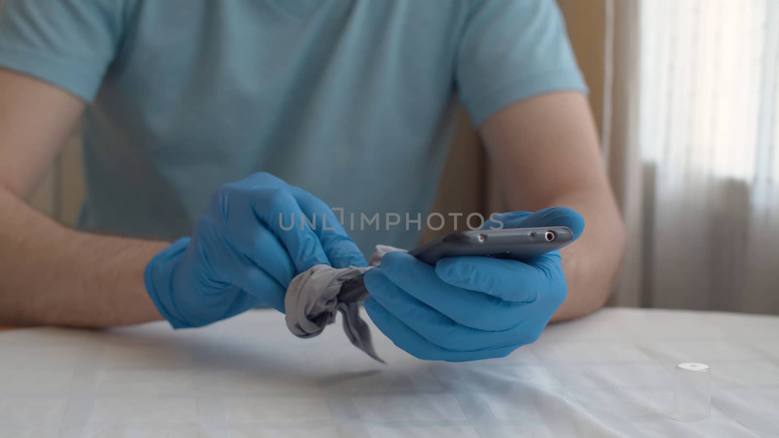 Close up male hands in protective gloves sanitaizing smart phone. He wipes it with a cloth. Hygiene during coronavirus epidemic. Concept of safety life.