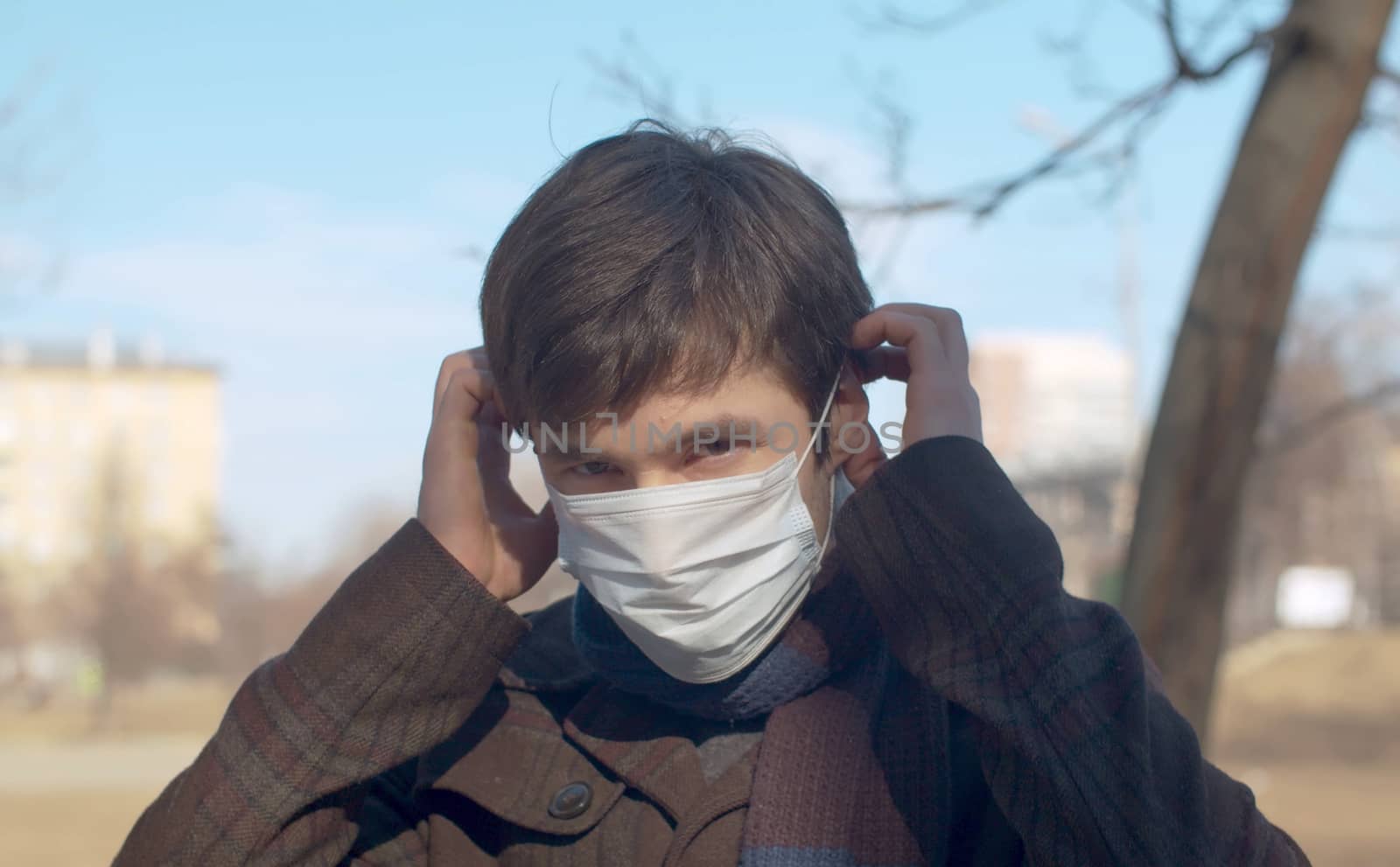 Close up portrait of a young handsome man putting on a protective mask outdoors in the city. Sunny sping day. Protect yourself and your loved ones. Covid-19 pandemic