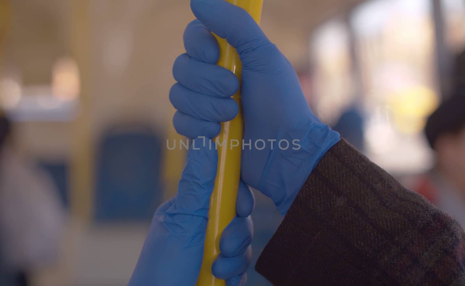 Close-up of a two people wearing a blue latex gloves holding pole in a public bus. Coronavirus epidemic in the city. Healthy and safety lifestyle concept.