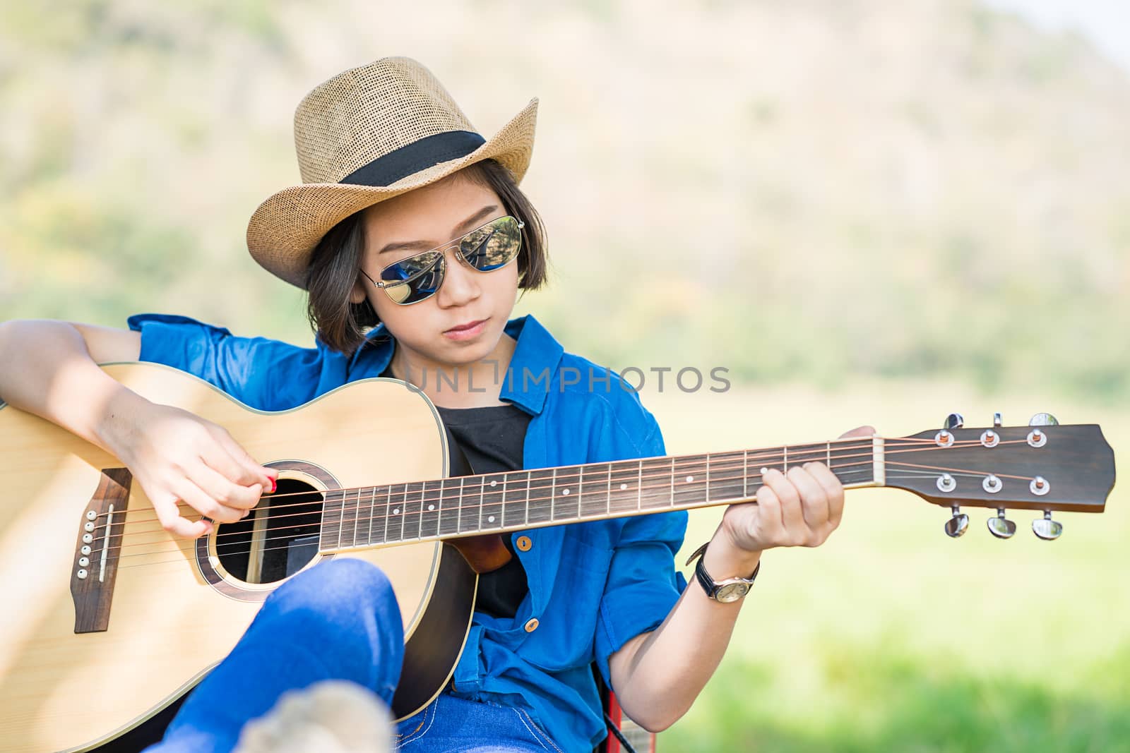 Close up young asian women short hair wear hat and sunglasses playing guitar in countryside Thailand