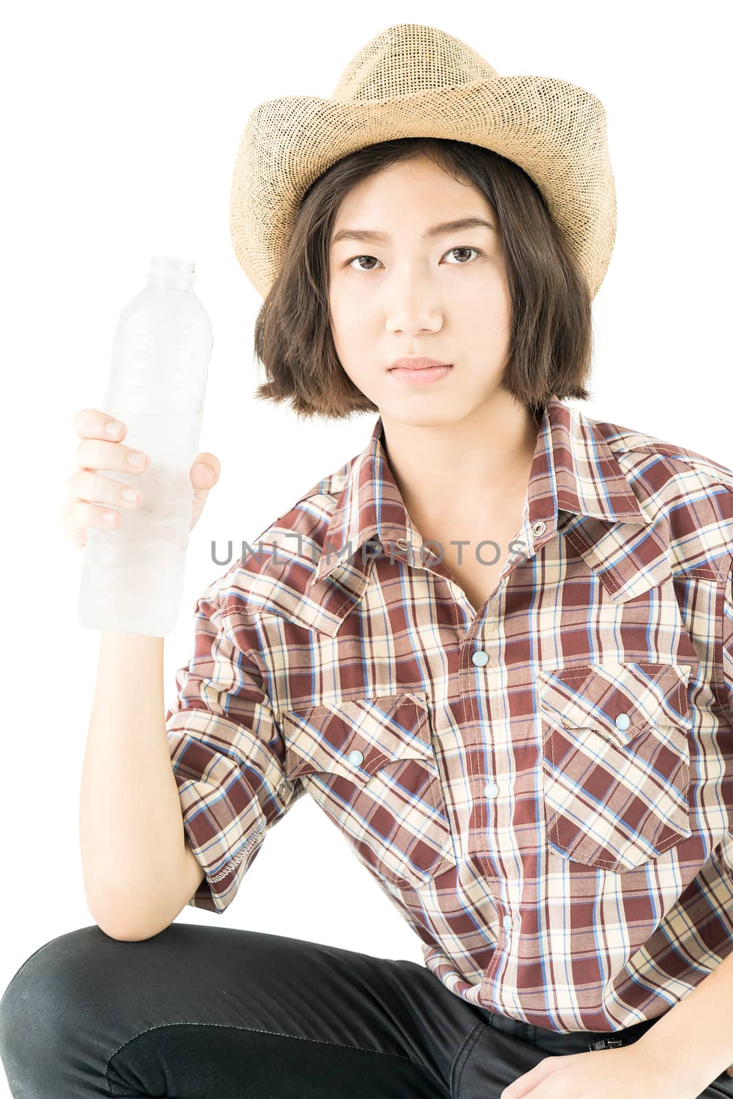 Young pretty woman in a cowboy hat and plaid shirt holding a water bottle isolated on white background