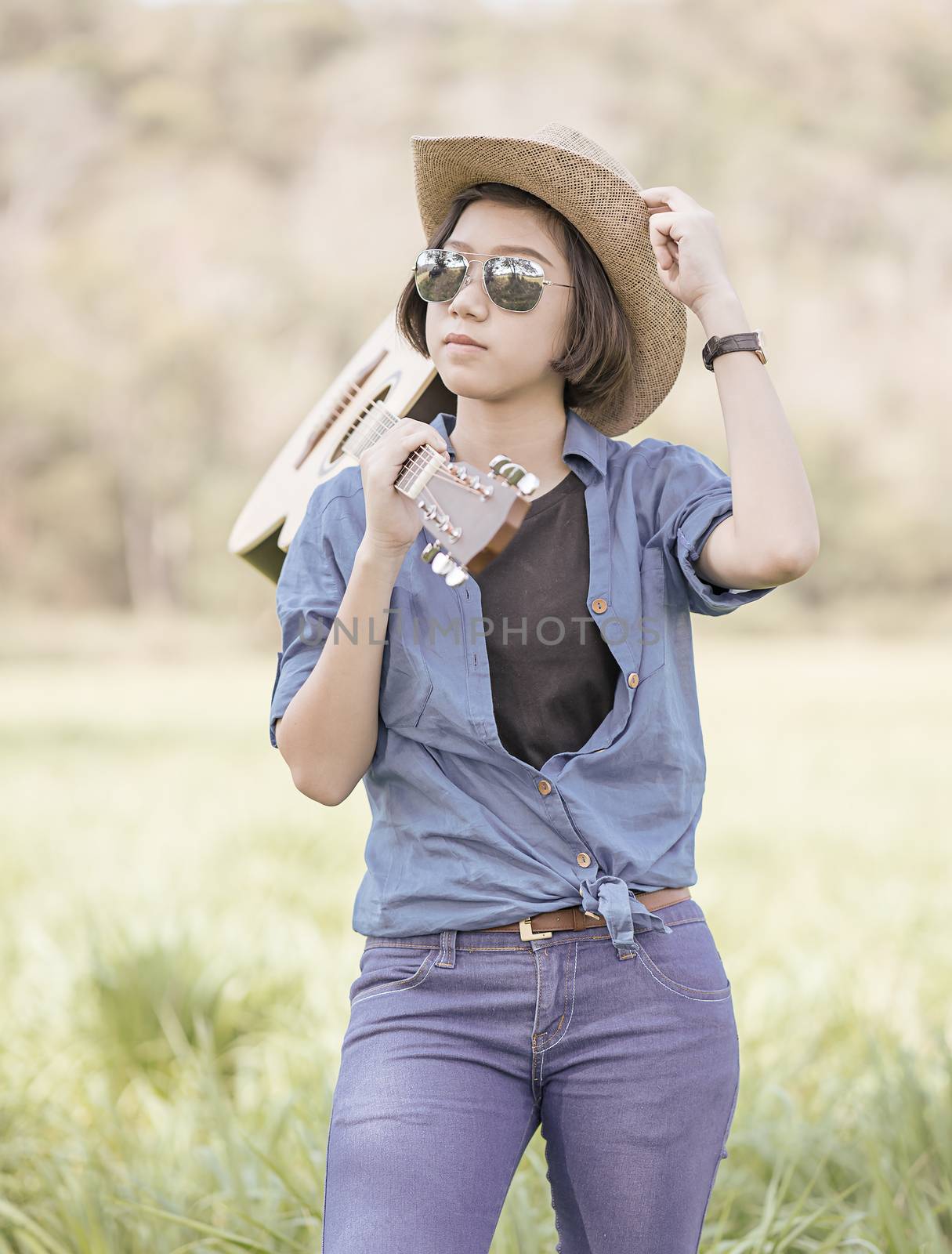 Woman wear hat and carry her guitar in grass field  by stoonn