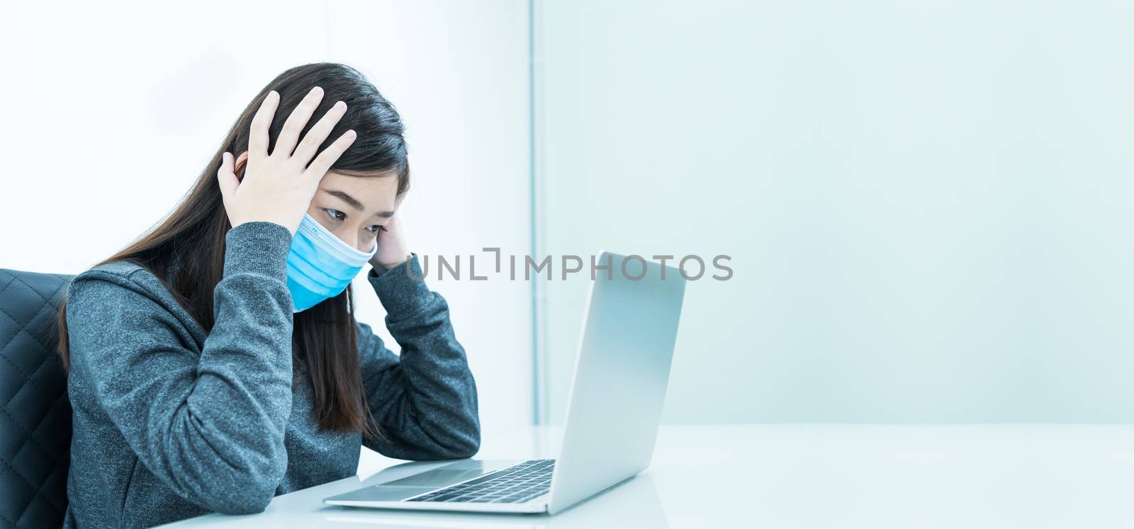 Woman using a laptop on the desk with headache and wearing  protective mask for protection against virus Covid-19