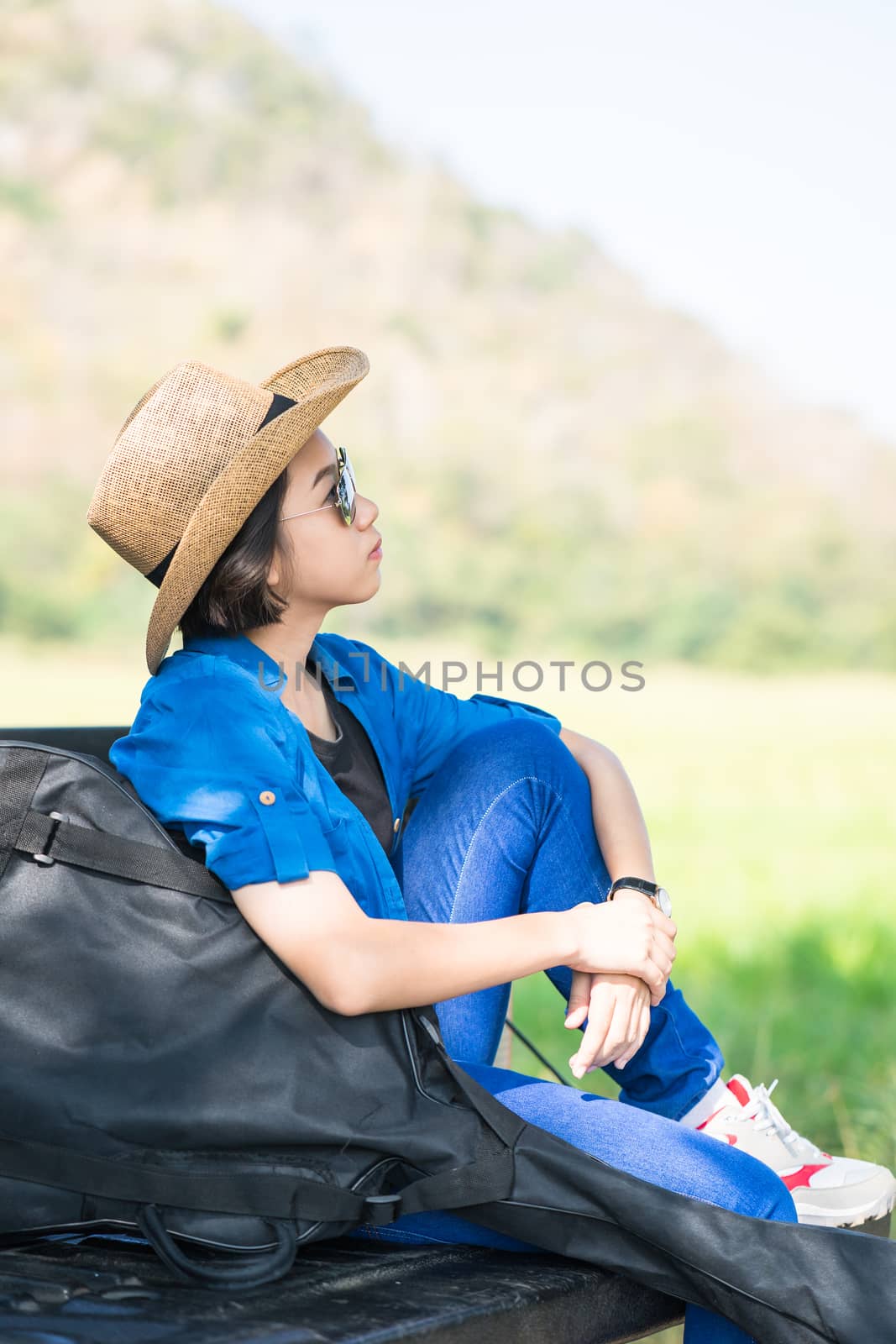 Young asian women short hair wear hat and sunglasses carry her guitar bag ,sit on pickup truck in countryside Thailand