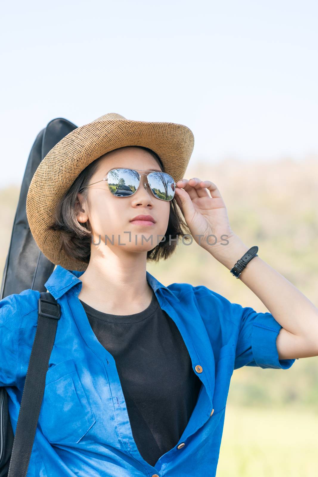 Young asian woman short hair wear hat walking and carry her guitar bag along in countryside Thailand