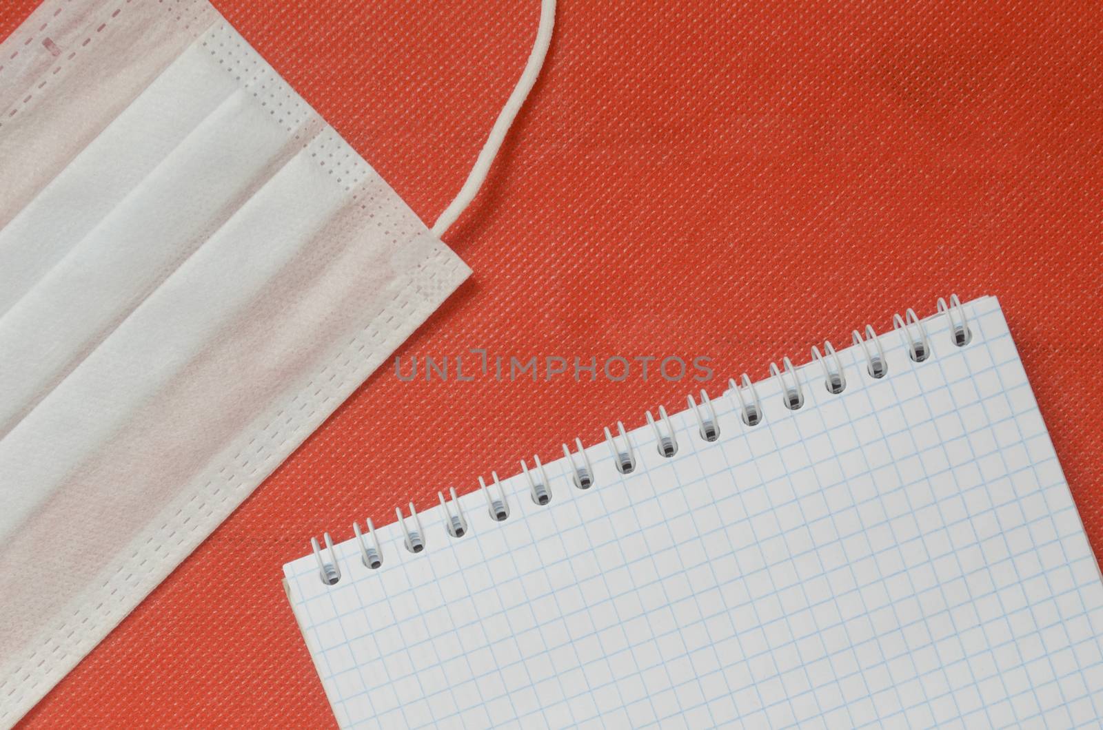 Top view, medical mask, and emty notepad on red background. by andre_dechapelle