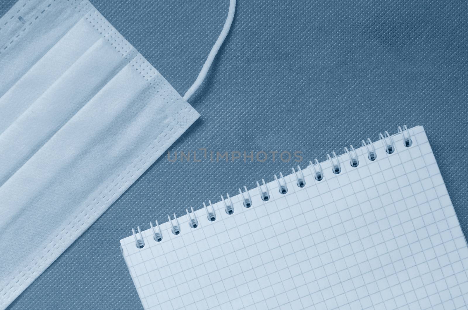 Concept of a coronavirus pandemic.2020 Classic blue tone. Top view, medical mask, and emty notepad on classic blue background