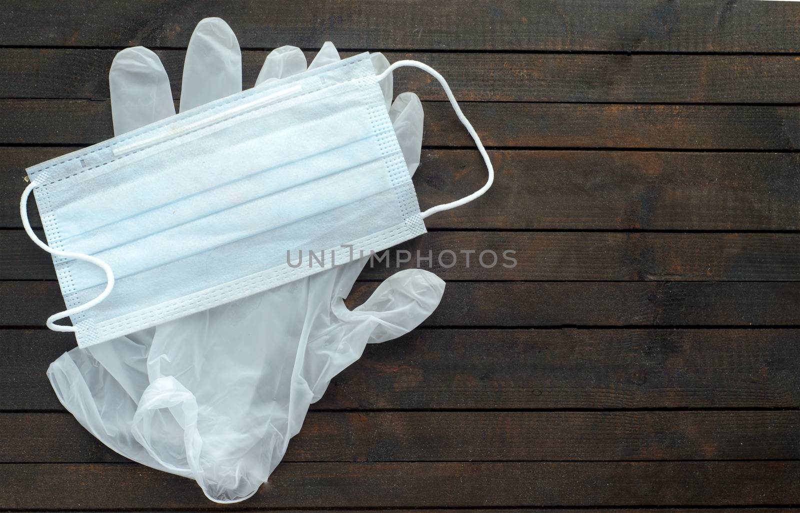 White medical mask and disposable gloves on dark wooden background.Gloves for protection against coronavirus. by andre_dechapelle