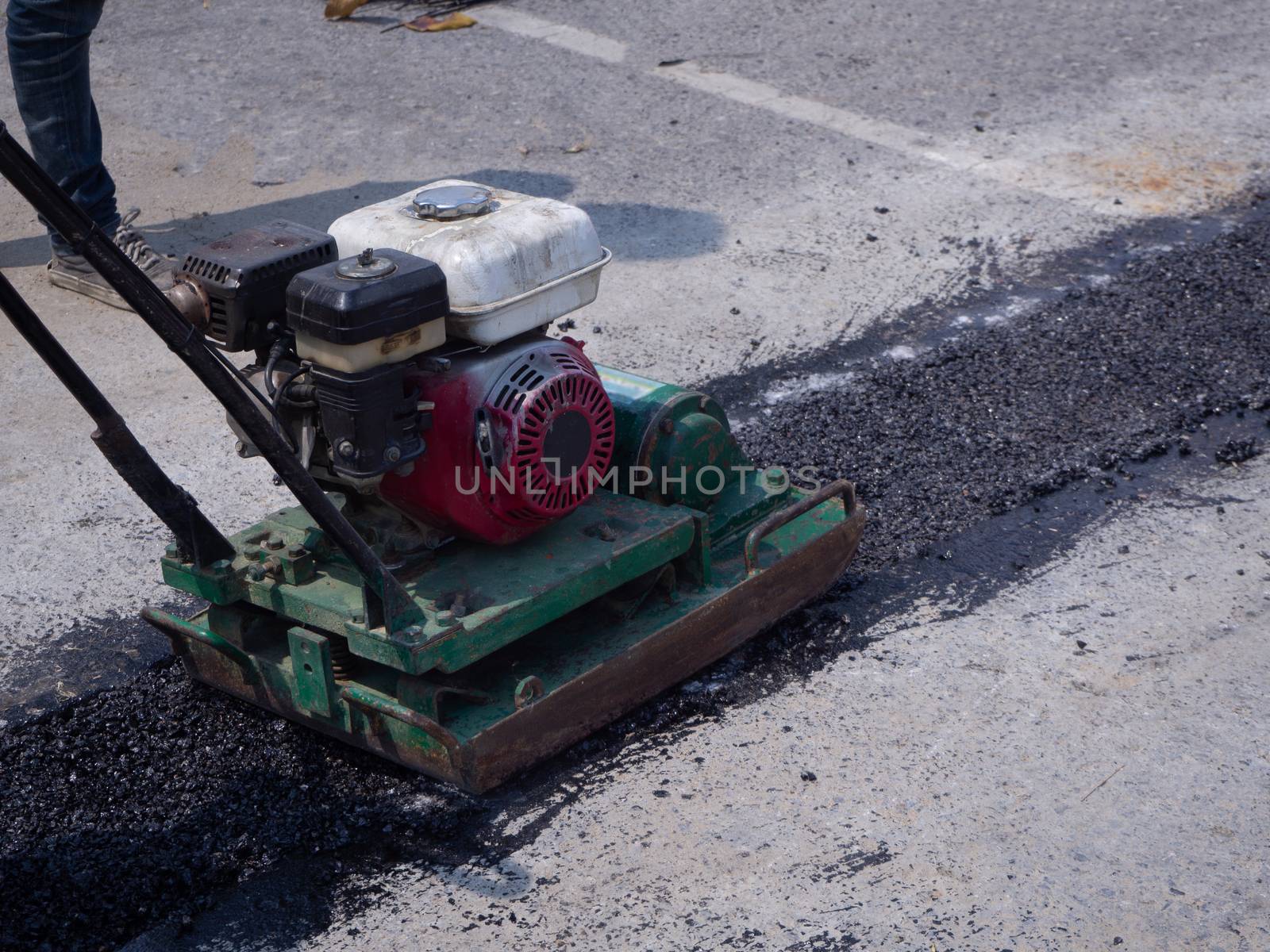 Worker use vibratory plate compactor compacting asphalt at road repair