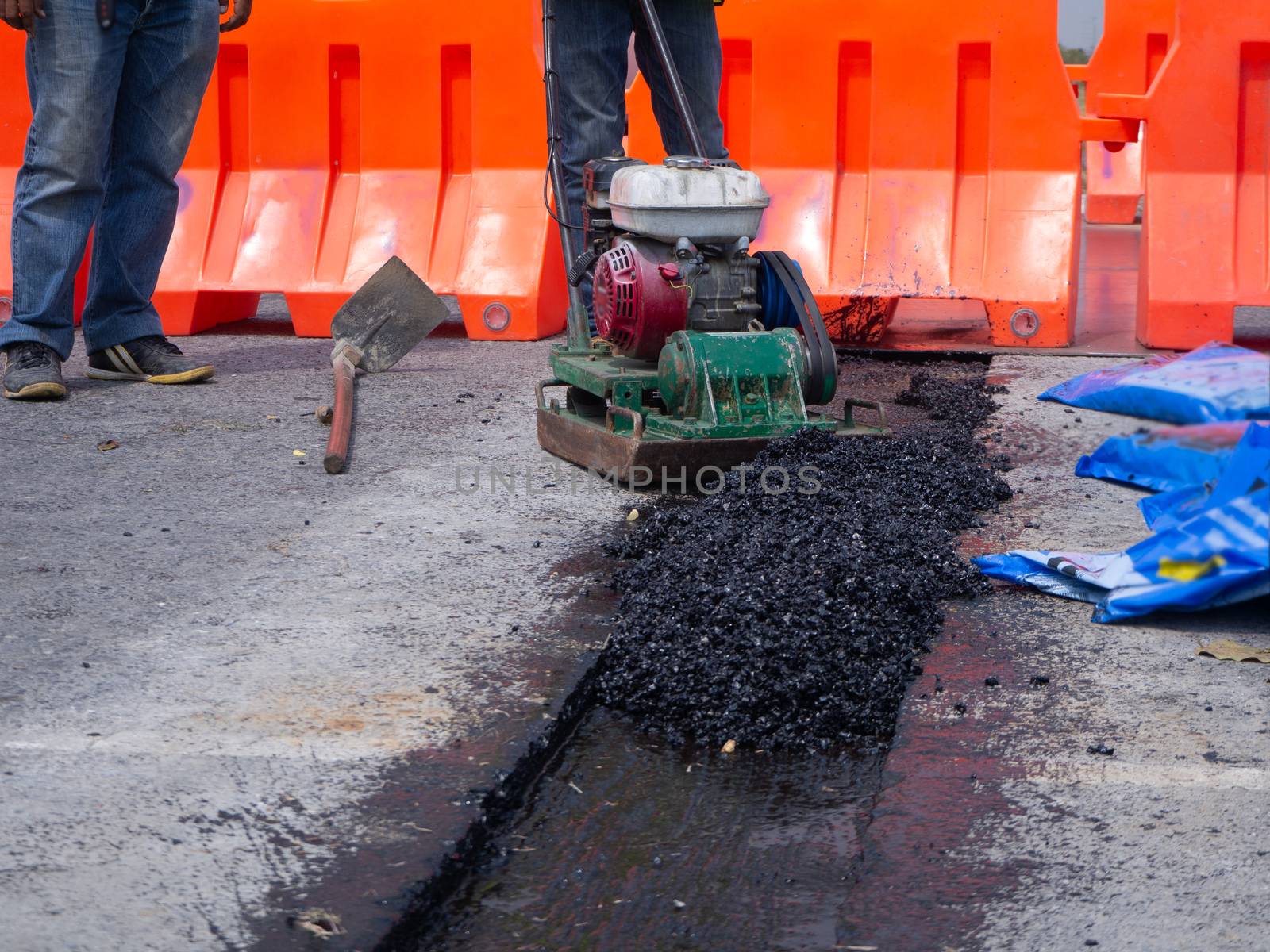 Worker use vibratory plate compactor compacting asphalt at road repair