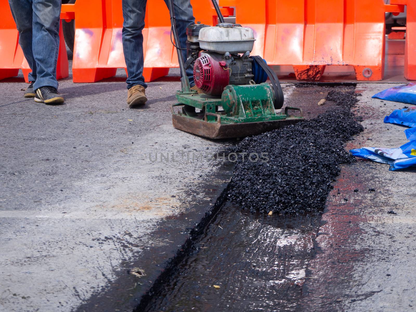 Worker use vibratory plate compactor compacting asphalt at road repair