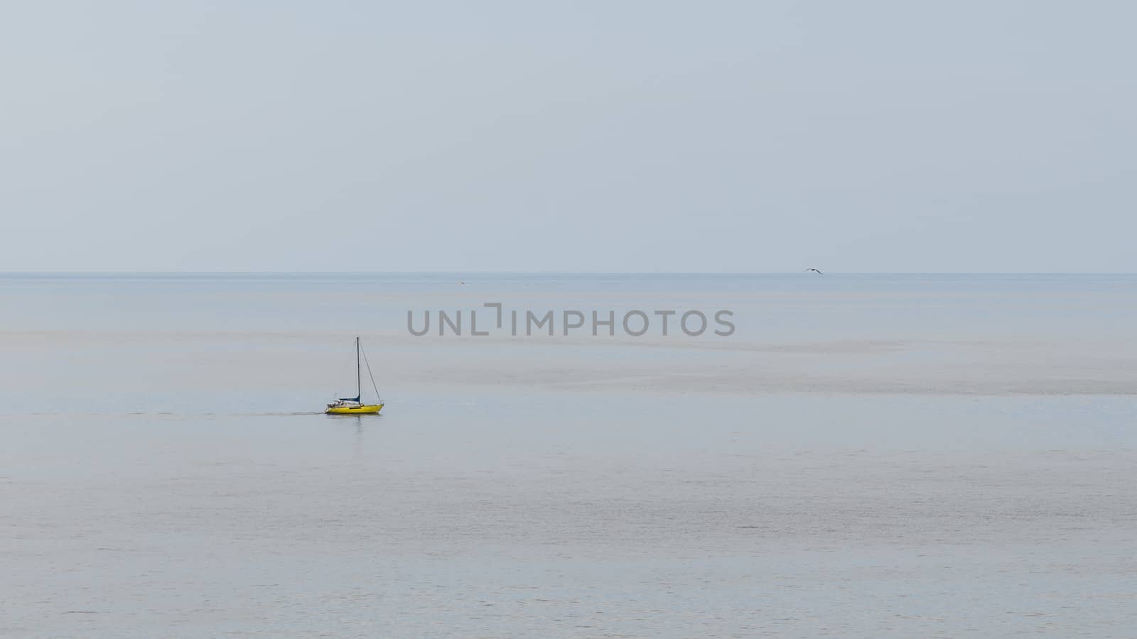 Yellow boat with its sails gathered up and stopped in a totally calm sea