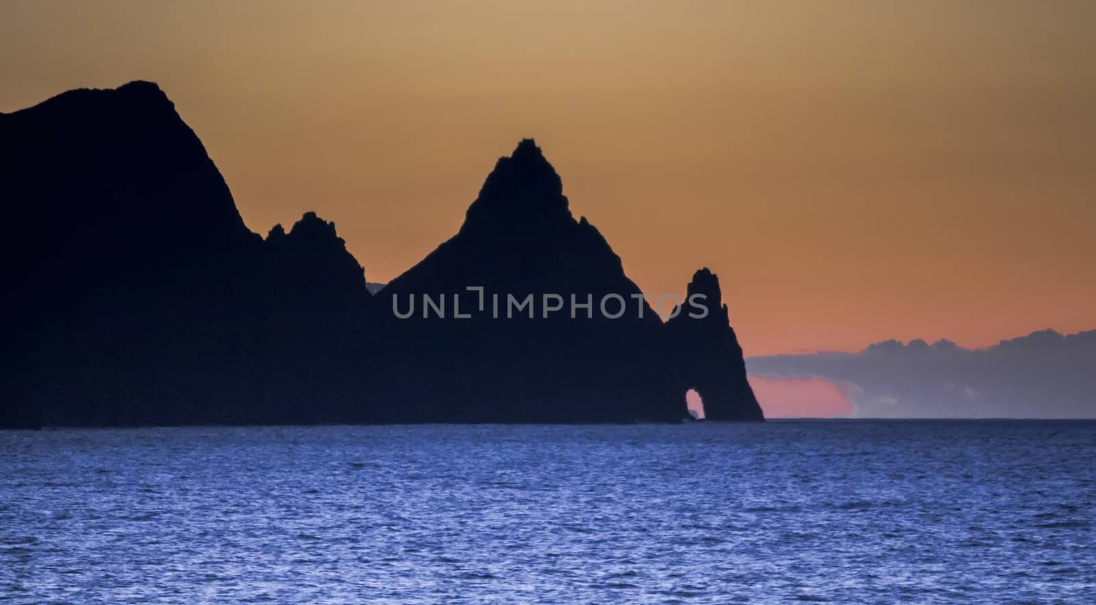 Sunset on the island of Madeira with the rocks of the coast and silhouette, the orange sky and the intense blue water