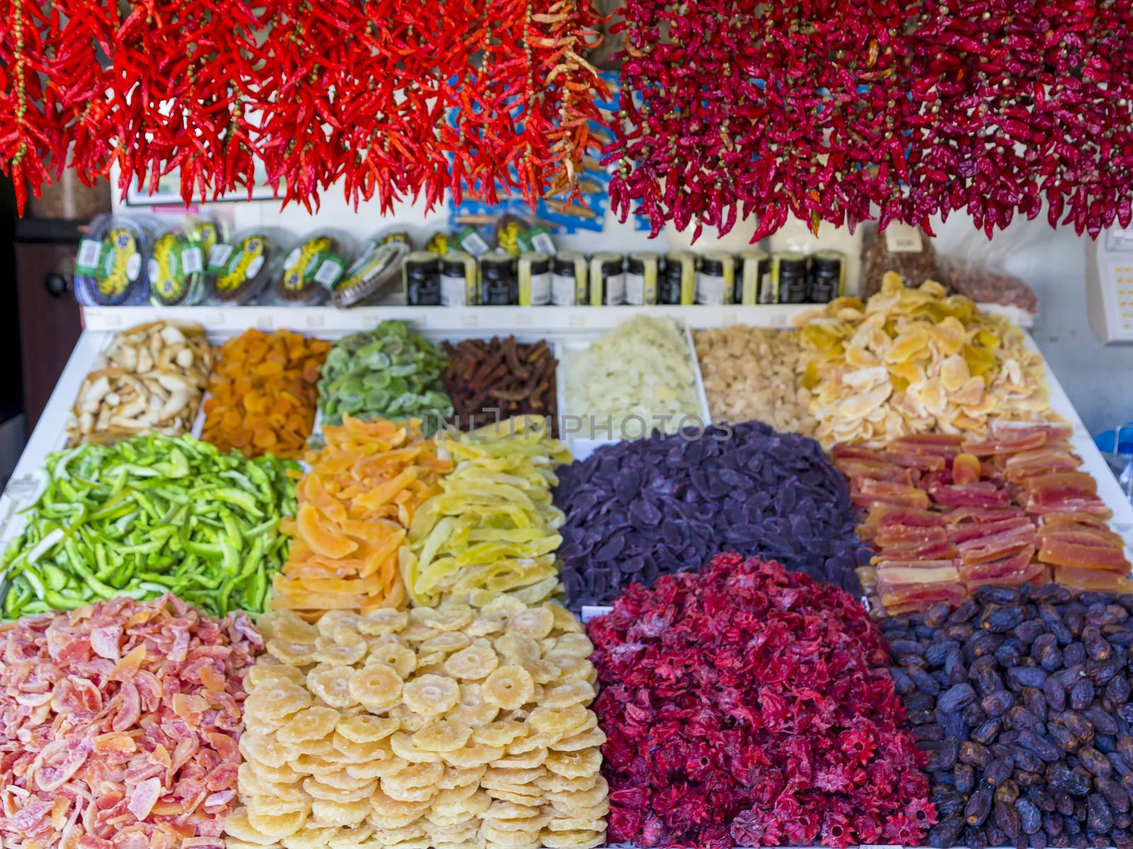Chillies and paprika hanging over vegetables and dried fruit at a market stall.