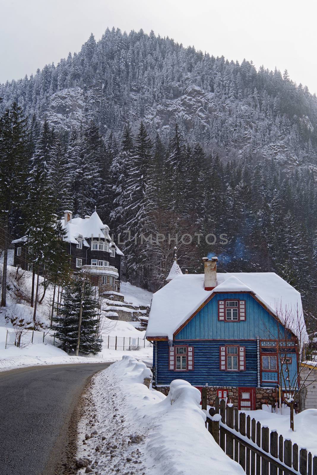 Winter scene in Red Lake Resort (Romania), snow covered houses and forest near road.