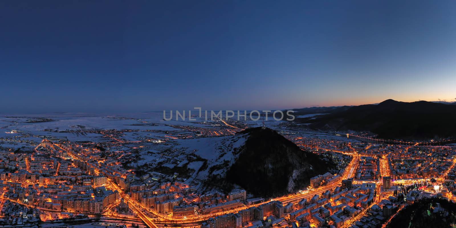 Drone view of night city lights and the mountains behind, Aerial landscape of Piatra Neamt in Romania, winter scene.