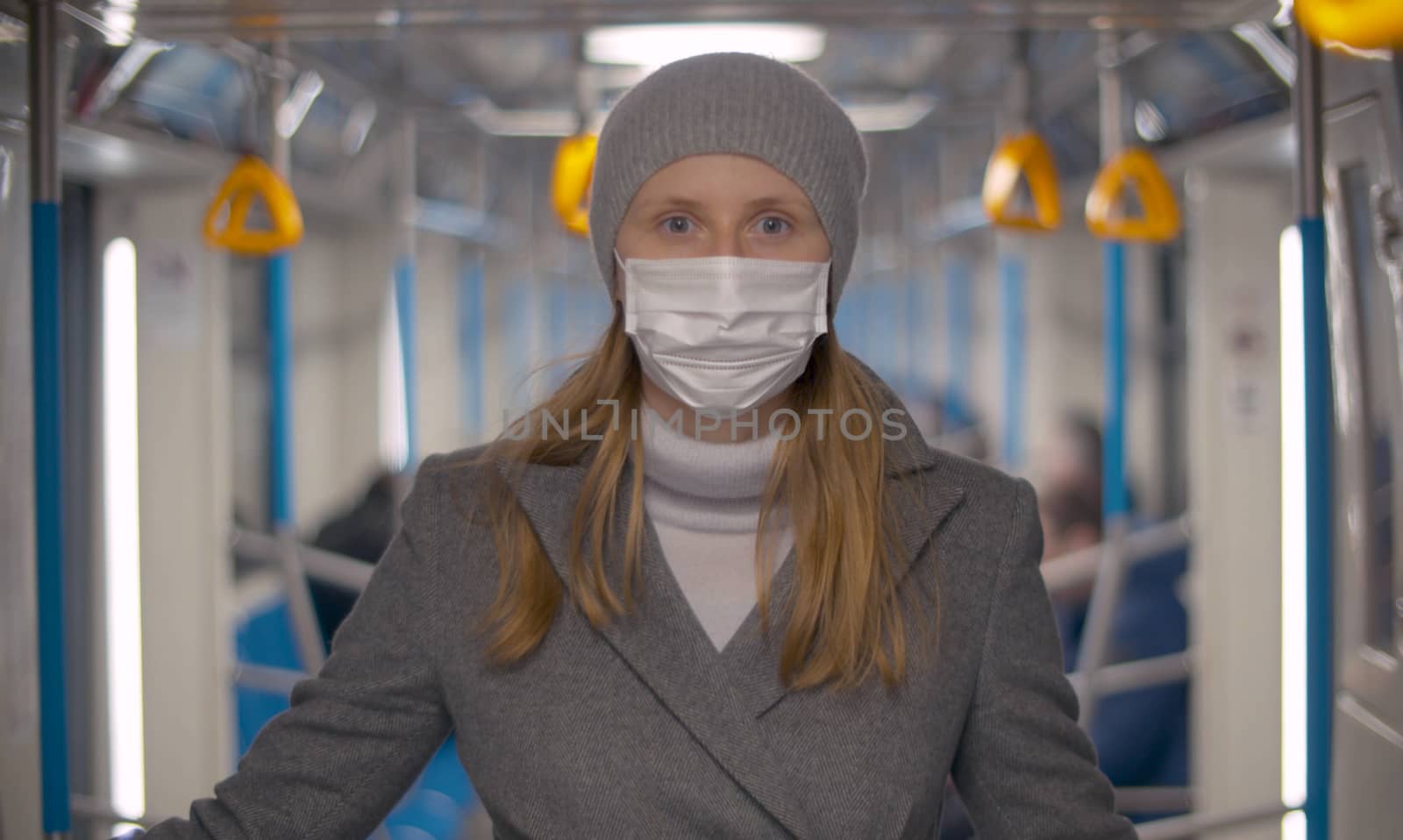 Close up portrait of young woman in protective mask in the subway car. Blurry unrecognizable passengers. Healthy and safety lifestyle concept. Covid-19 pandemic