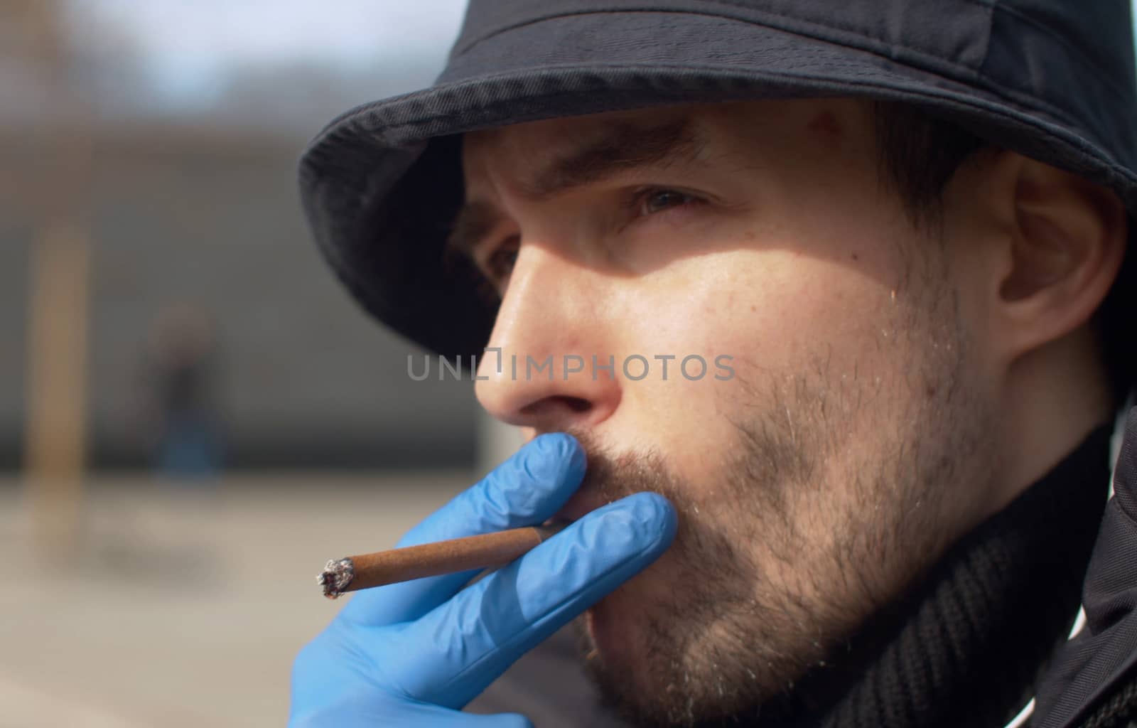 Close up portrait of a young man smoking a cigarette in protective gloves outdoors. Coronavirus epidemic. Concept of health and safety life. COVID-19 pandemic