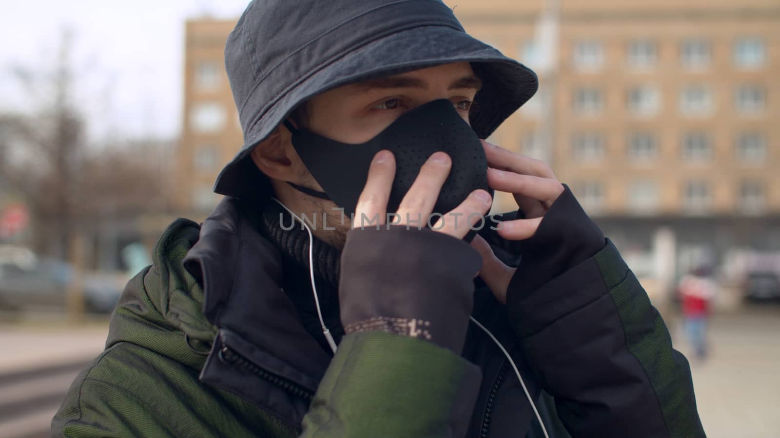 Close up portrait of a young man putting on a reusable face protective mask outdoors. Coronavirus epidemic in Moscow. Concept of health and safety life. COVID-19 pandemic