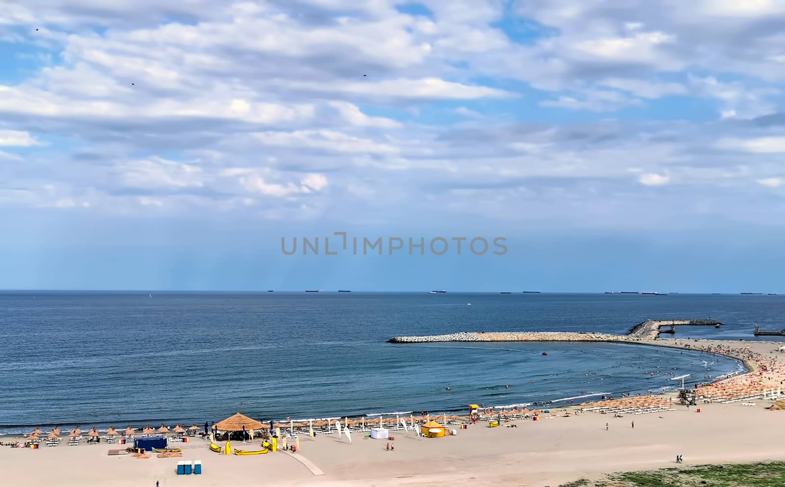 Summer beach with sun umbrellas and stone wave breaker in the sea