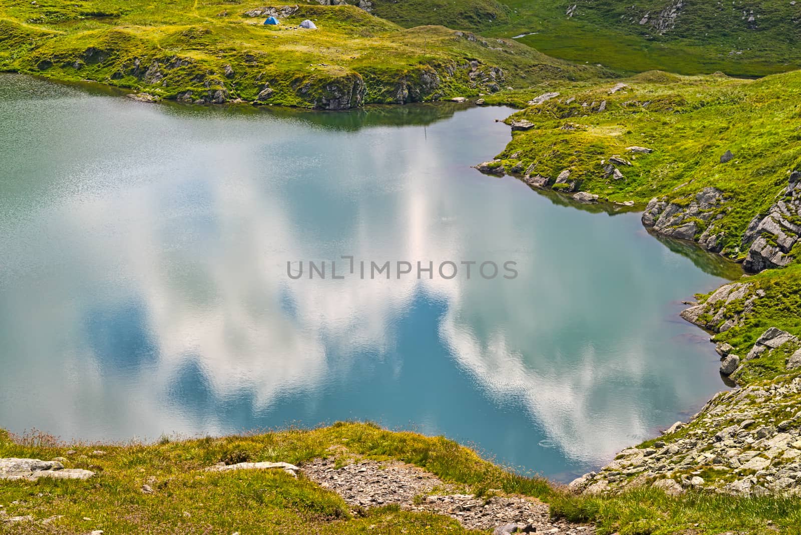 Reflecting clouds and sky in summer mountain lake, Capra lake in Romanian Carpathians