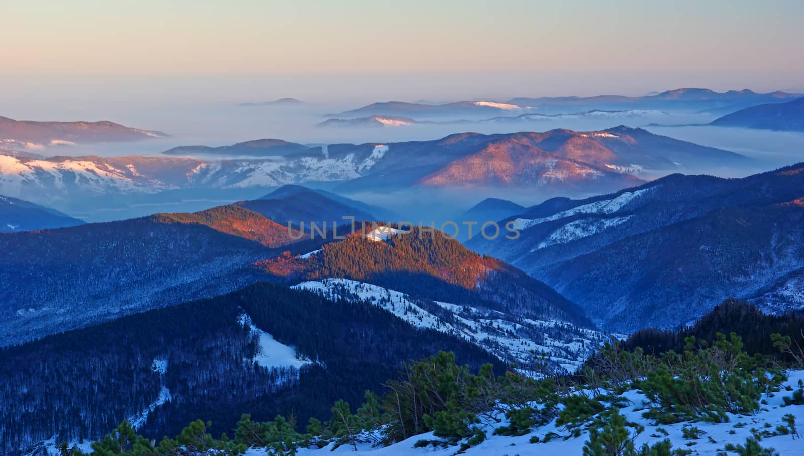 Sunset landscape over misty valley in Romanian Carpathians, Ceahlau mountain winter scene