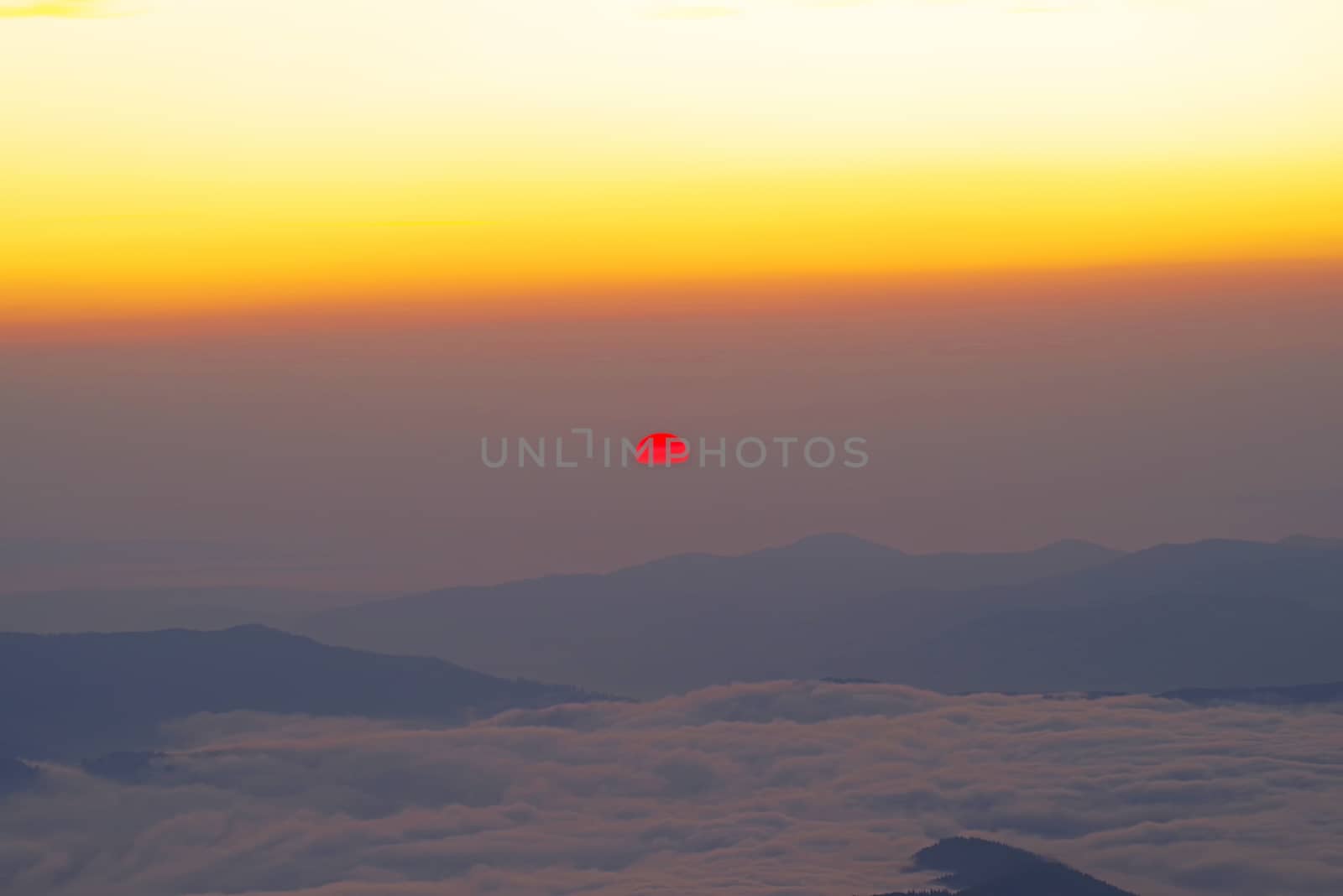 Red sun at sunrise from mountain top, low clouds and creast in valley