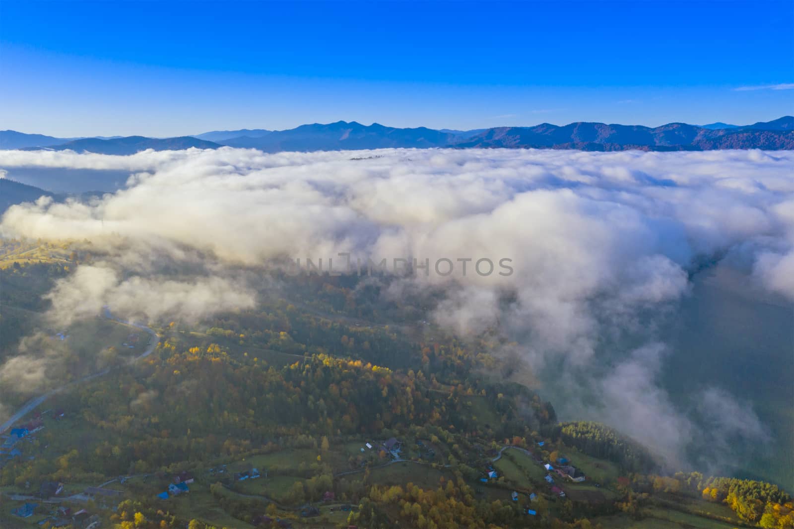 Mist clouds over the village and forest, aerial autumn landscape in Romanian Carpathians.