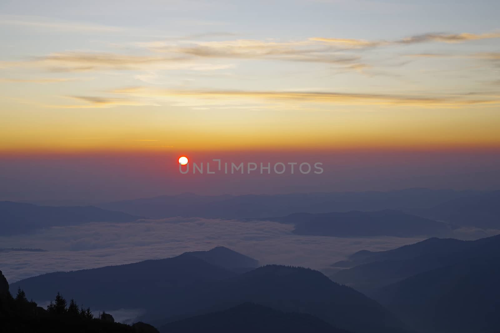 Sunrise landscape, sun appear at horizon over the crest, low clouds in the valley