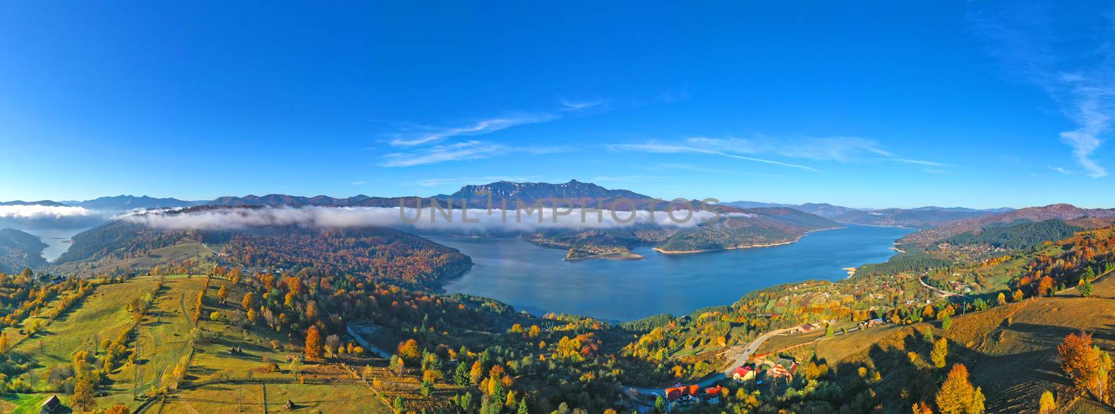 Aerial view of autumn mountain panorama in Romanian Carpathians mist layer over the lake and colored forest.