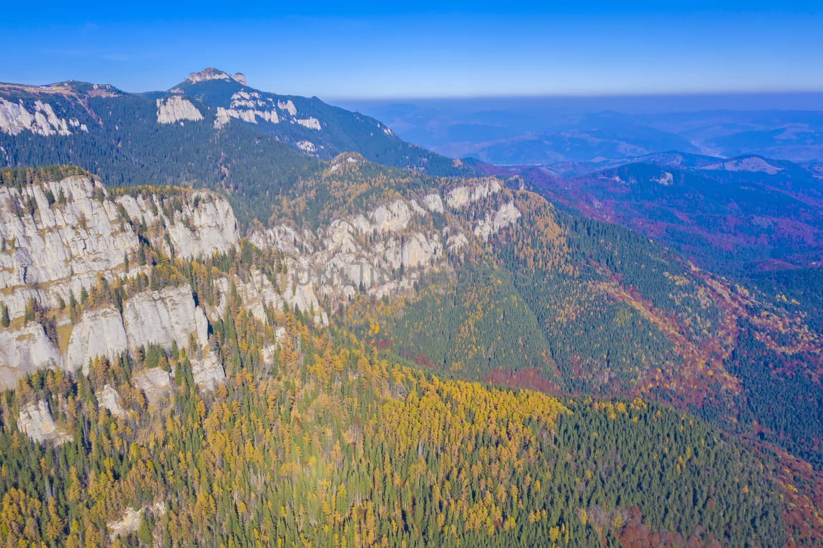 Autumn rocky mountain viewed from above in Romanian Carpathians, aerial view of Ceahlau mountain, beautiful colored forest