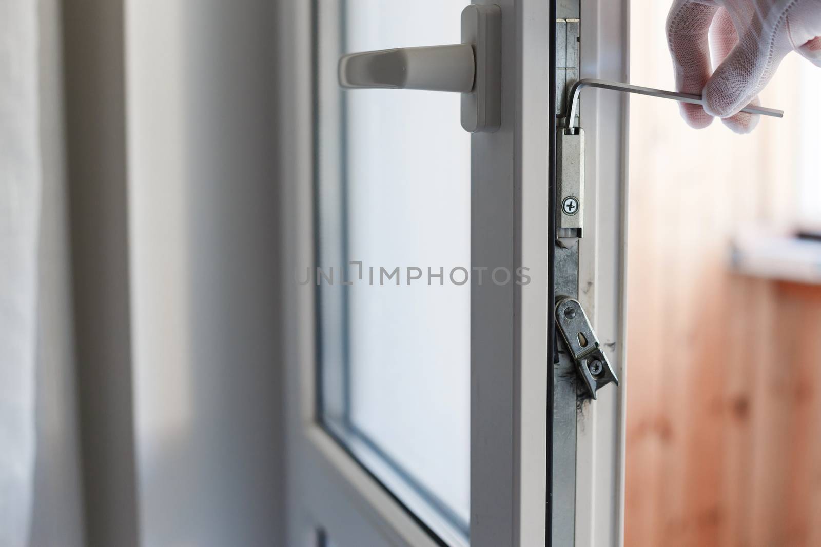 Man's hand makes adjustment of hardware of the uPVC door mechanism with an allen key