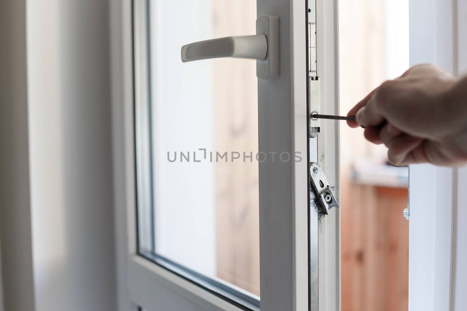 Man's hand uses screwdriver for adjustment of hardware of the uPVC door mechanism