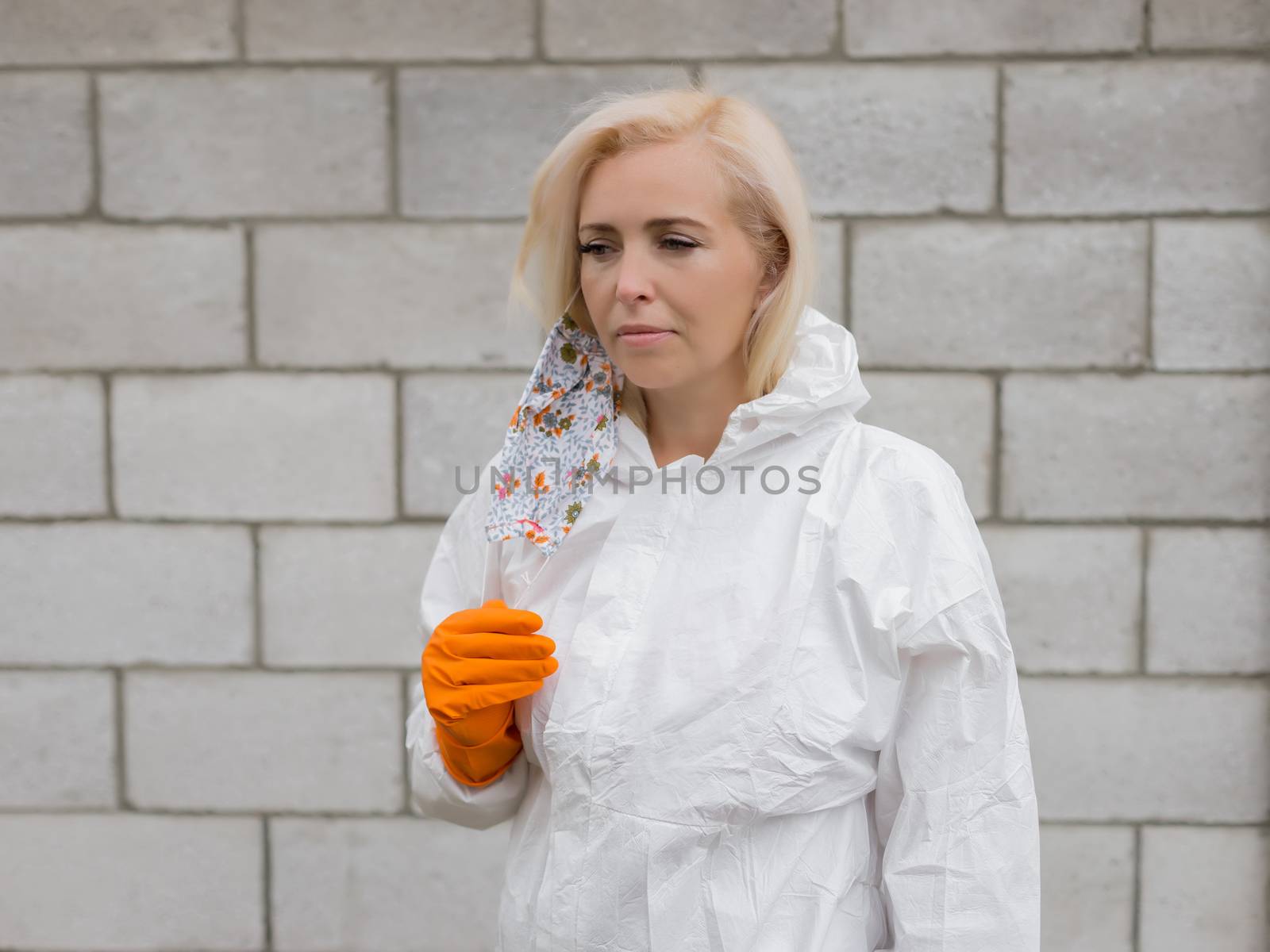 Woman in black mask, white protective suit taking off mask