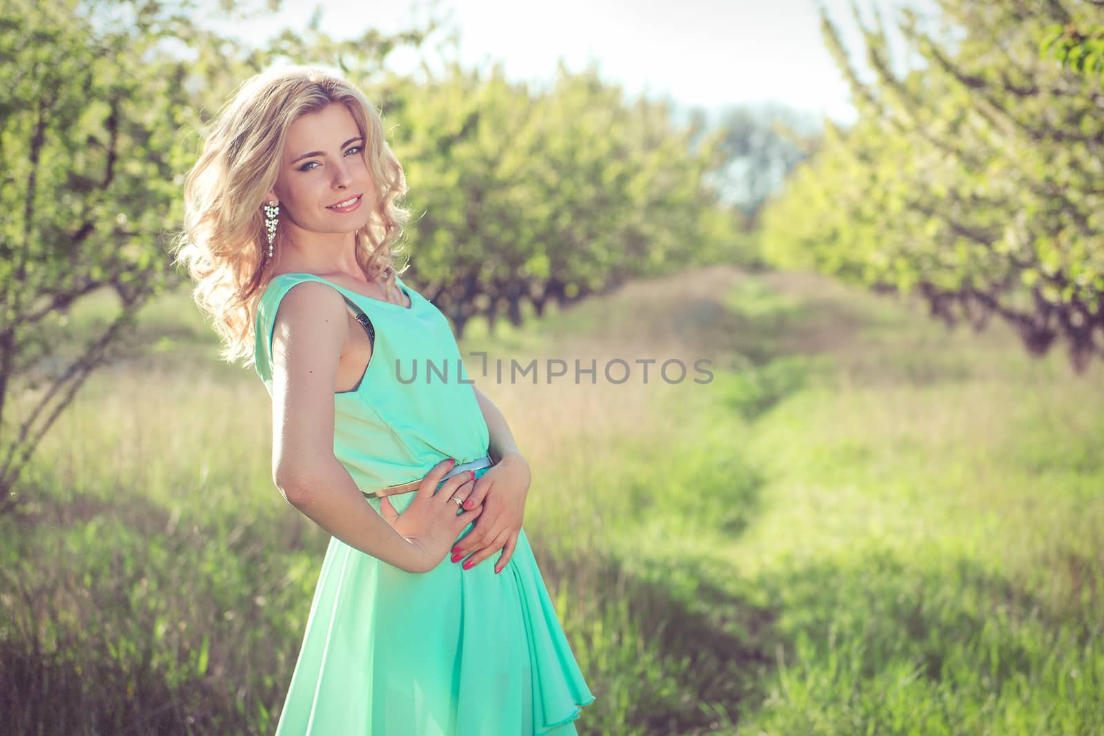 young blonde girl in a turquoise light dress walks in the spring garden