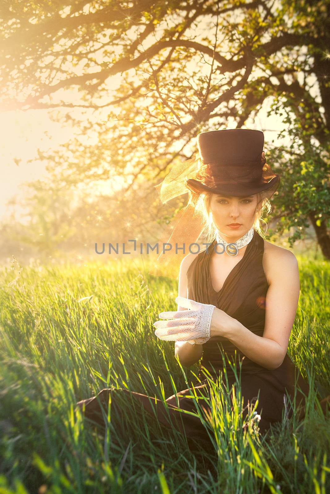 young blonde girl in a brown vintage dress and top hat reads a book in spring garden