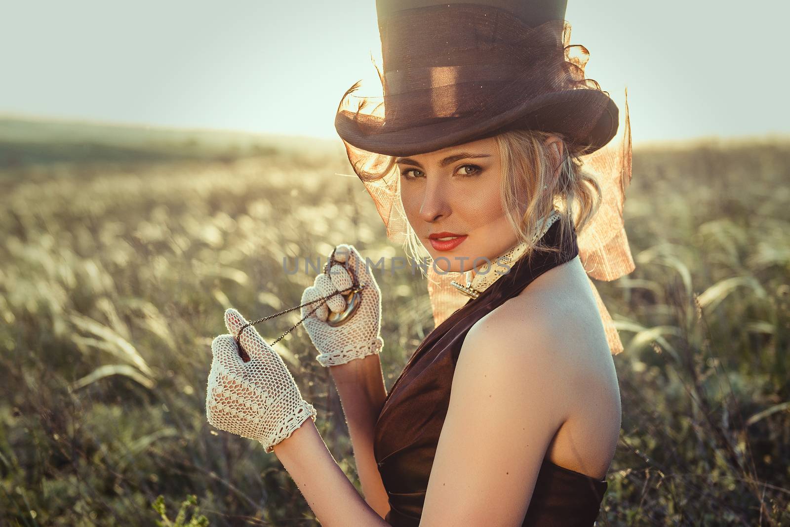 young blonde girl in a brown vintage dress and top hat in a feather grass