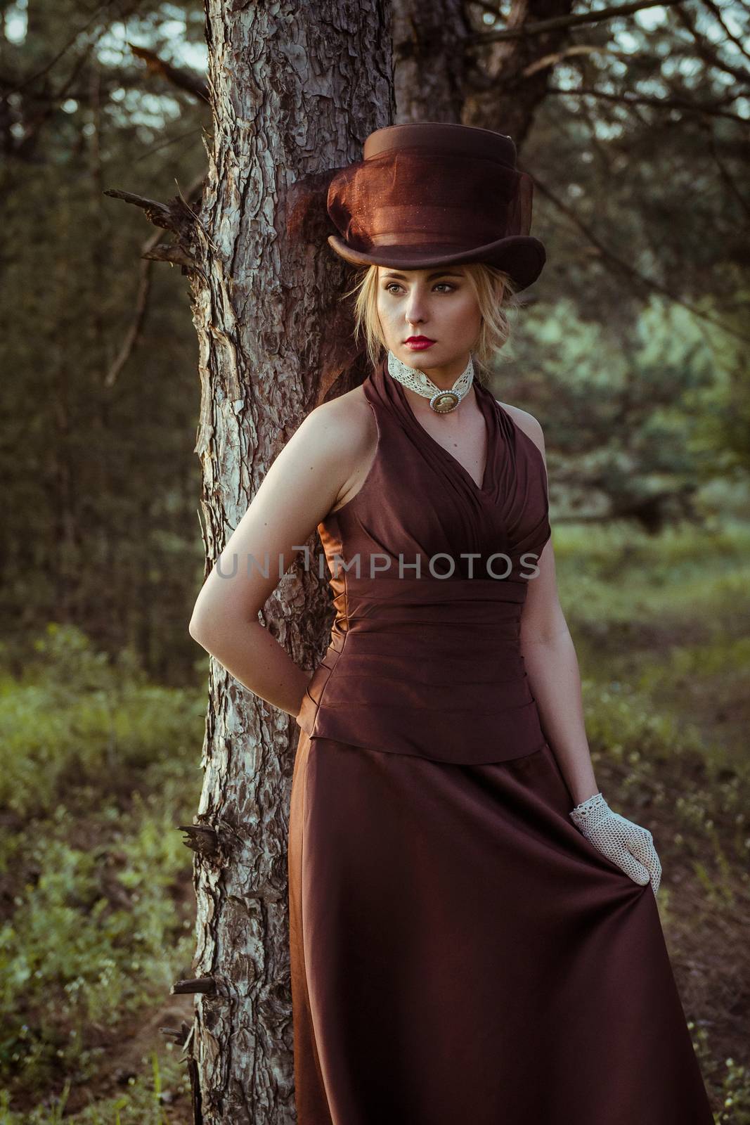 young blonde girl in a brown vintage dress and top hat in the forest