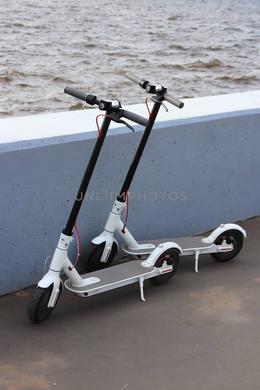 Two white electronic scooters parked on the embankment of the Neva River