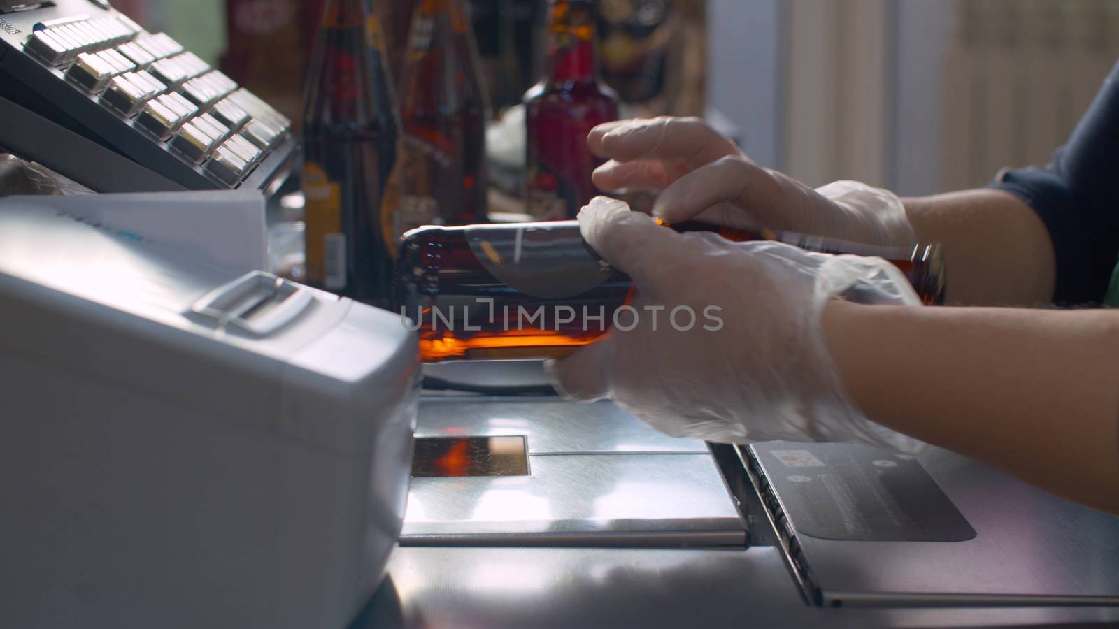 Close up checkout counter in the supermarket during coronavirus epidemic. Cashier's hands in protective gloves scans beer. COVID-19 pandemic