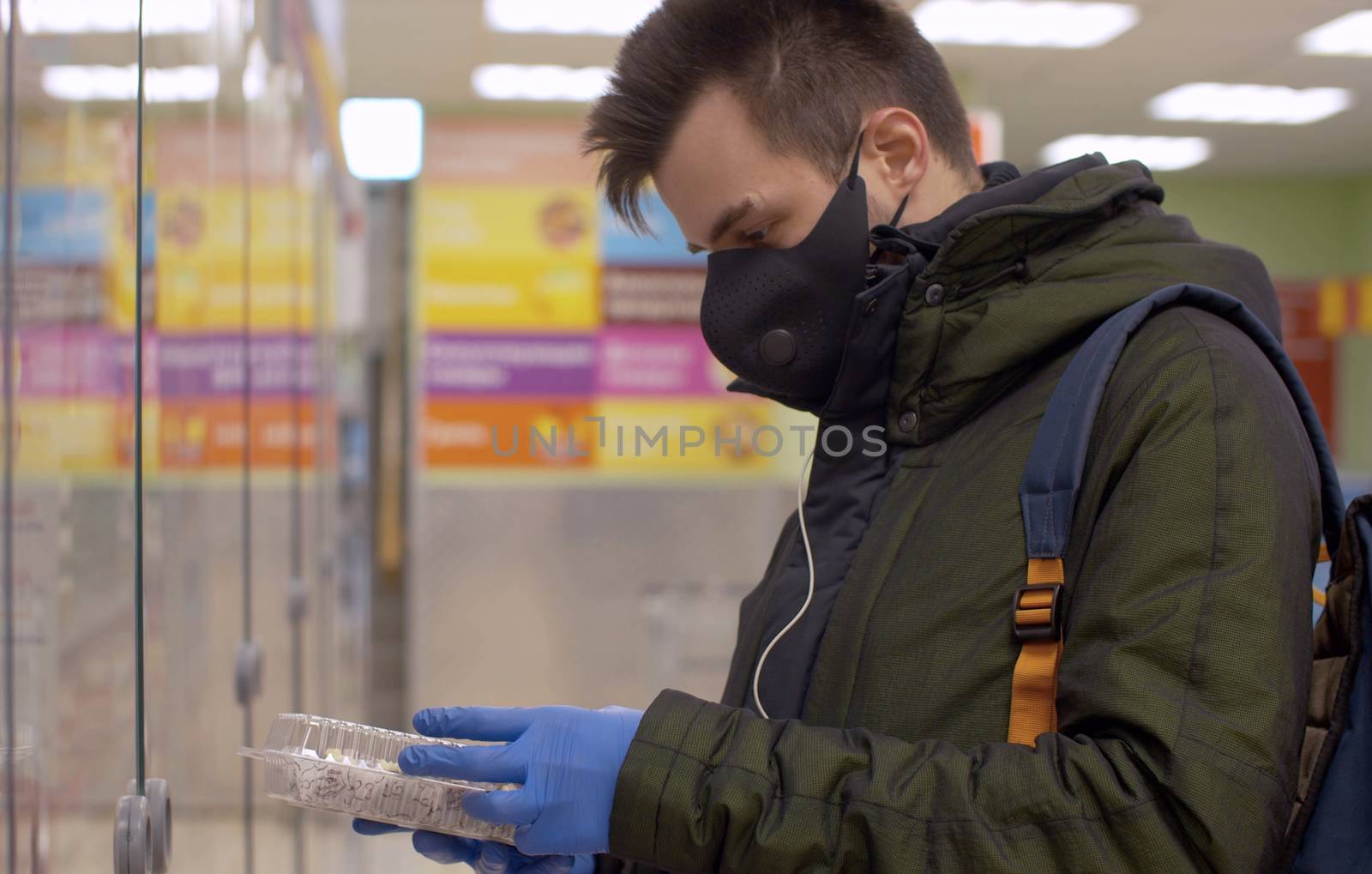 A man in a protective mask and gloves choosing food in the supermarket. Coronavirus epidemic in the city. COVID-19 pandemic