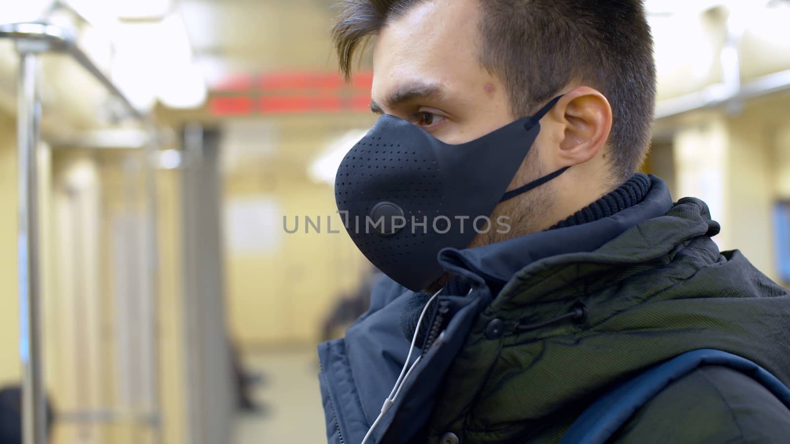 Close up portrait of a young man in reusable protective mask inside subway car. Blurry passengers. Coronavirus epidemic precautions. Healthy lifestyle concept. COVID-19 pandemic