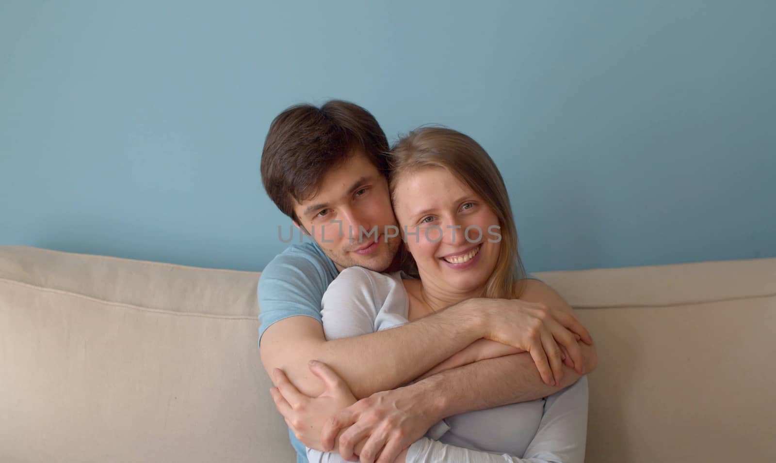 Nice happy family in love hugging in bright room. Young caucasian couple sitting on the sofa and enjoying togetherness