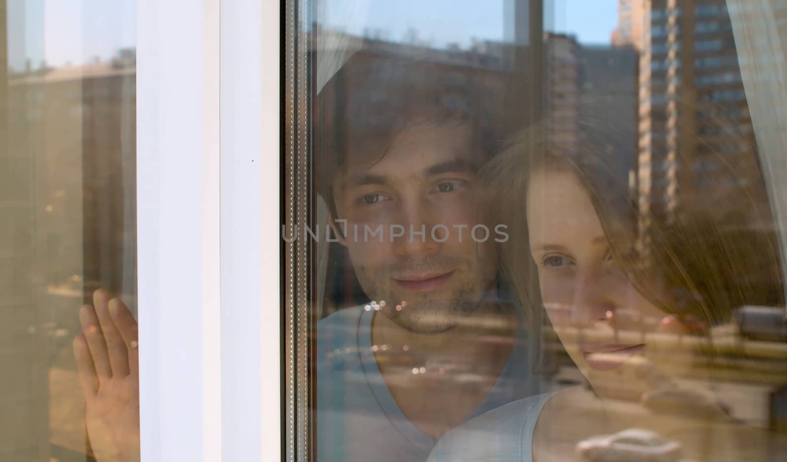 Young happy couple in love shooting through the window. They are looking outside. The window reflects houses and vehicles on the street