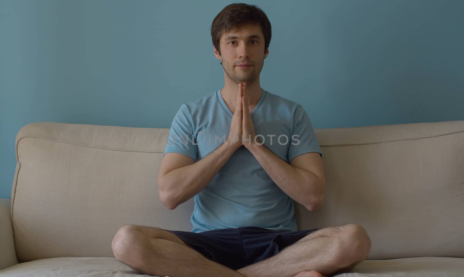 Portrait of young meditating man on blue background. The concept of meditation, relaxation, yoga, stress relief and inner peace and quiet