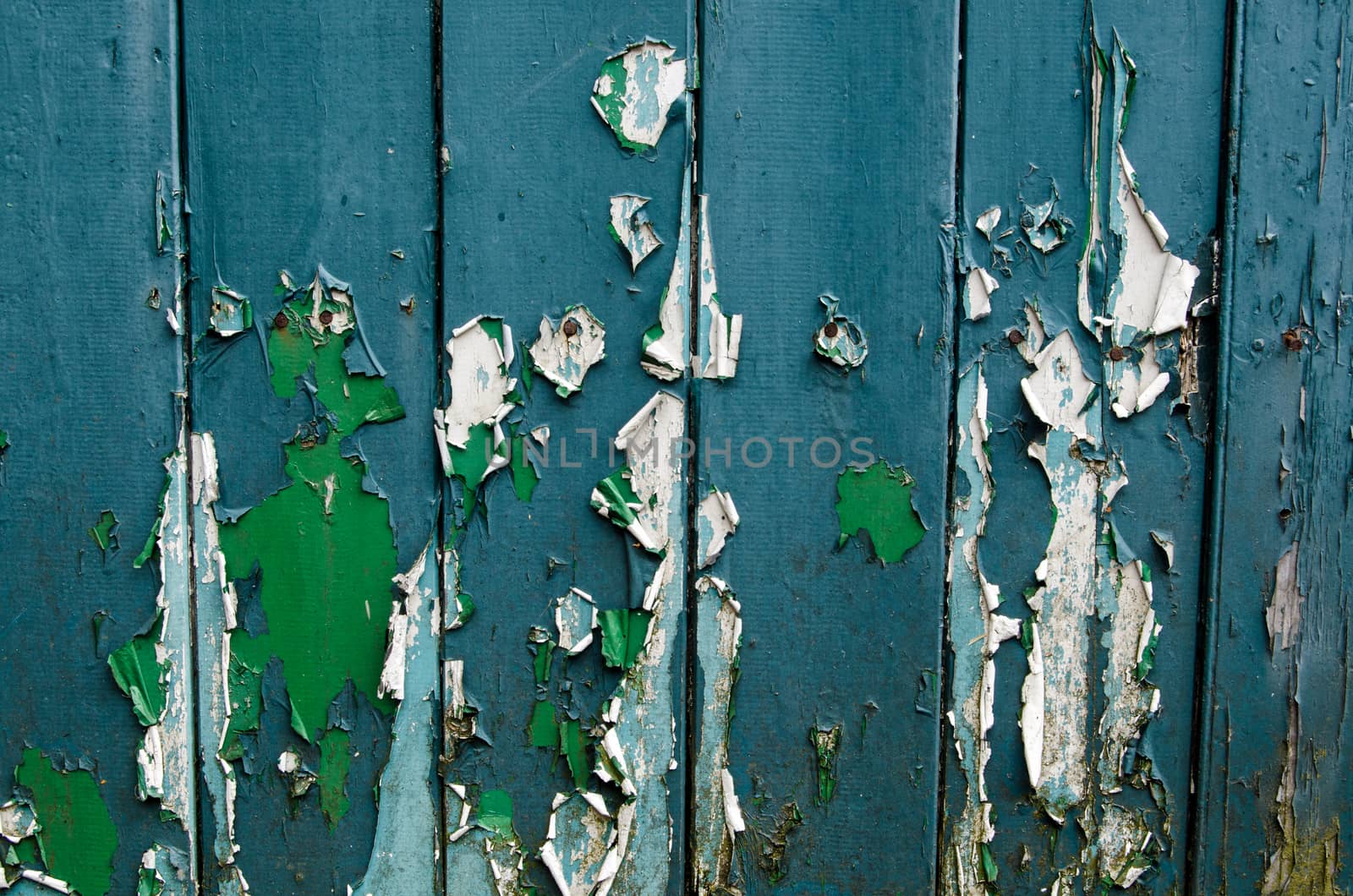 Peeling paint on a wooden door showing previous shades of green and blue that have been used in years past.